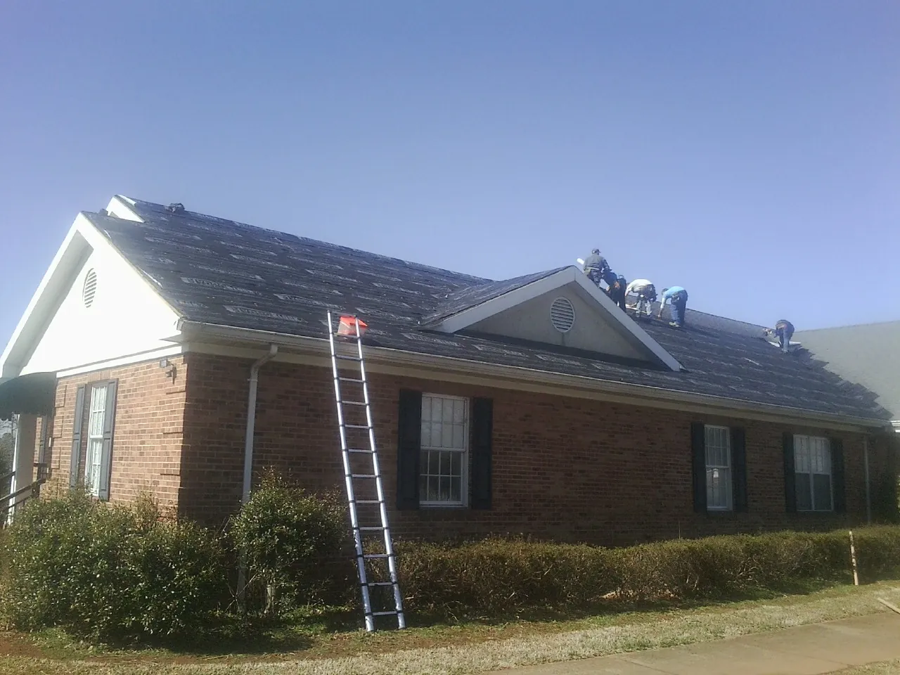 Crew tearing shingles off a brick ranch roof with a ladder set — Metal Roof Repair work by our crew in Eagle
