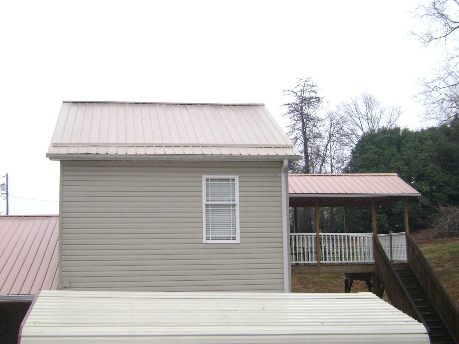 Tan metal roofs on a two story addition and attached porch, from a Roof Replacement job in Eagle